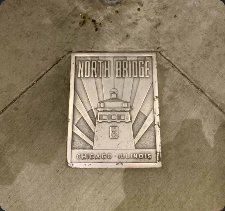 A cast North Bridge plaque set into the pavement, stained by rain — Chicago, Illinois