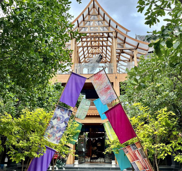 A timber arch hung with printed textiles, framed by trees — Kalm Village, Chiang Mai, Thailand